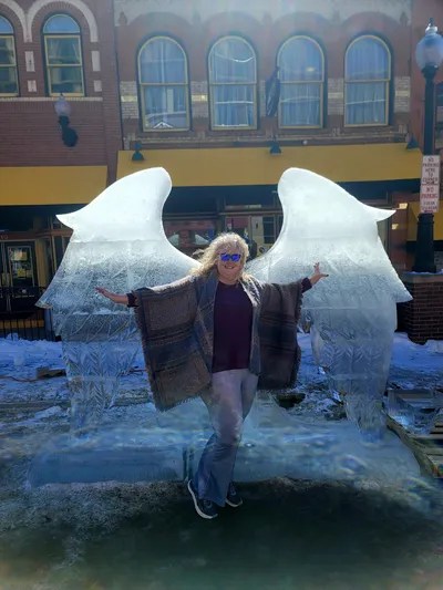 A photo of Patsy standing in front of angel wings carved out of ice.